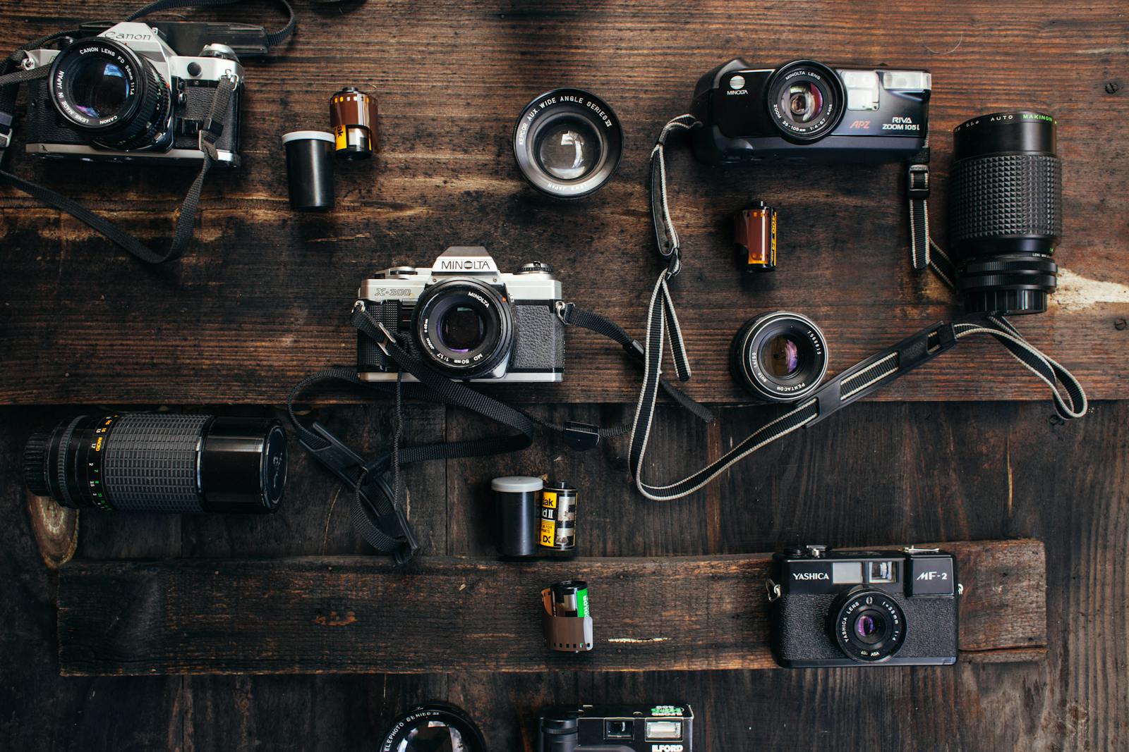 Overhead of retro photo cameras near various lenses and films on wooden surface