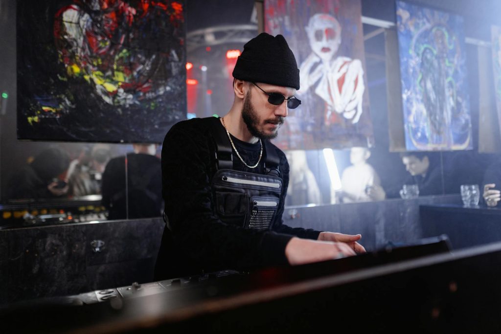 Energetic DJ in sunglasses spins tracks at a lively indoor club event with abstract art.
